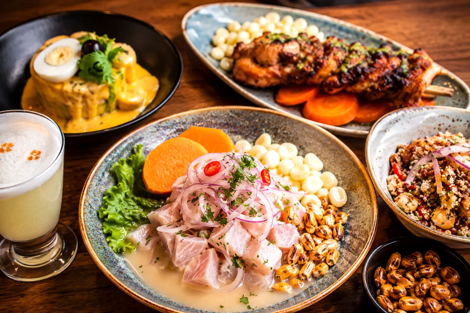 A spread of Peruvian dishes featuring fresh ceviche, causa rellena, anticuchos, cancha corn, and a frosty pisco sour.